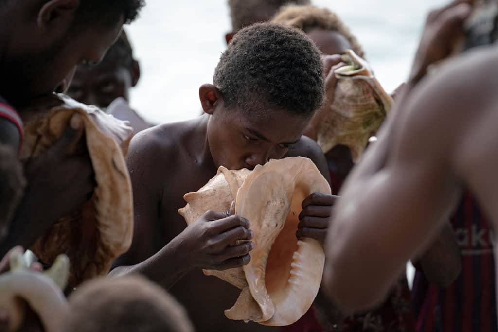 A Young Boy Blasts A Tune Through The Hollows Of A Conch Shell.