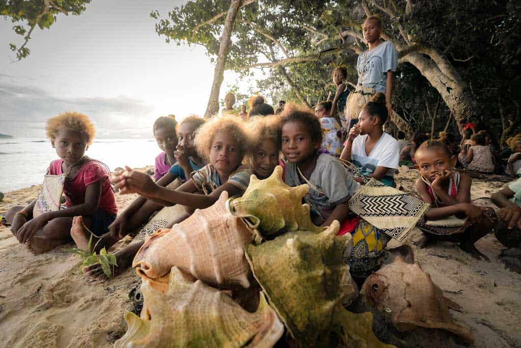 Young Kids Sit By The Conch Shells As The Sun Rises Behind Them.